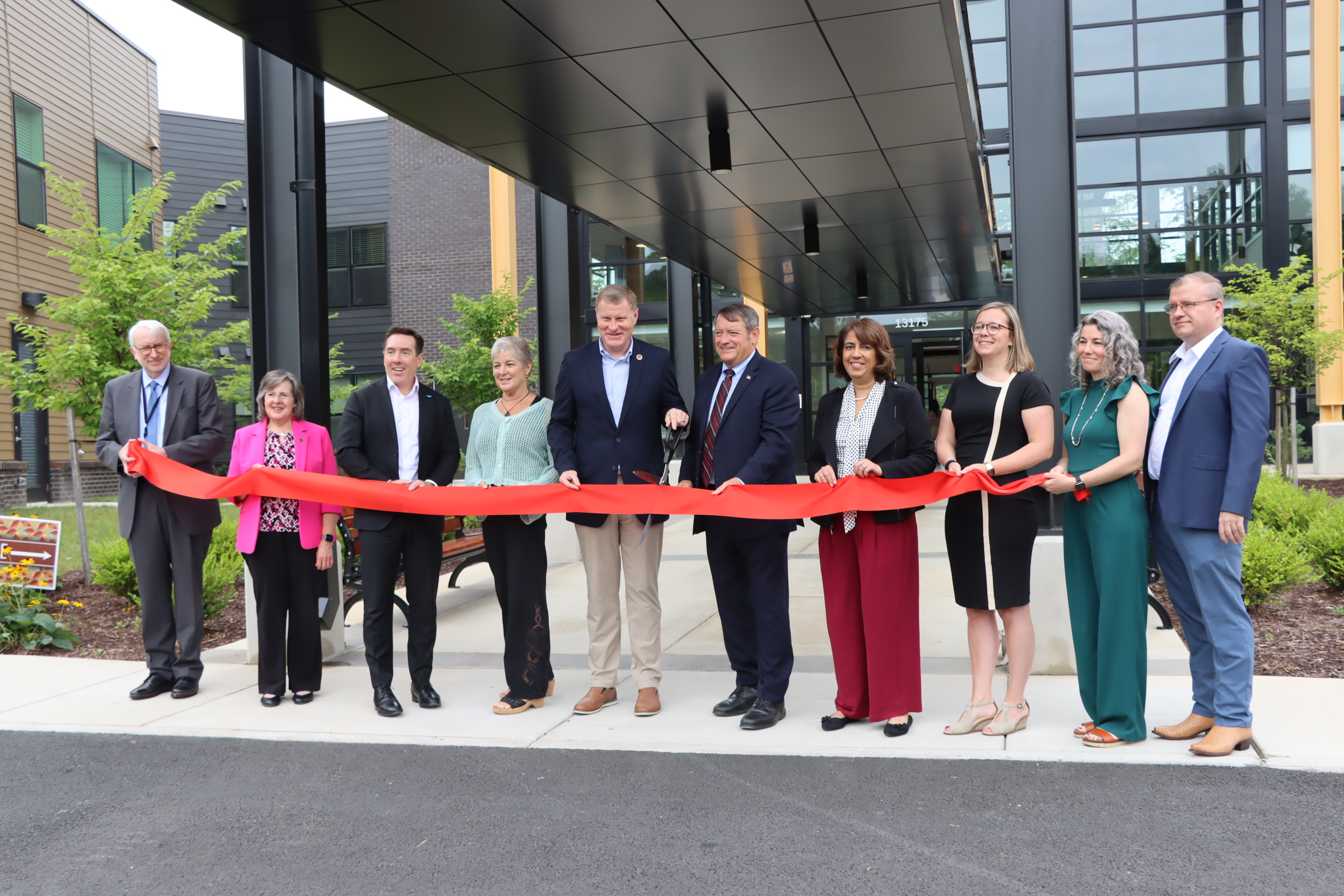 a photo of officials cutting a red ribbon in front of an apartment community